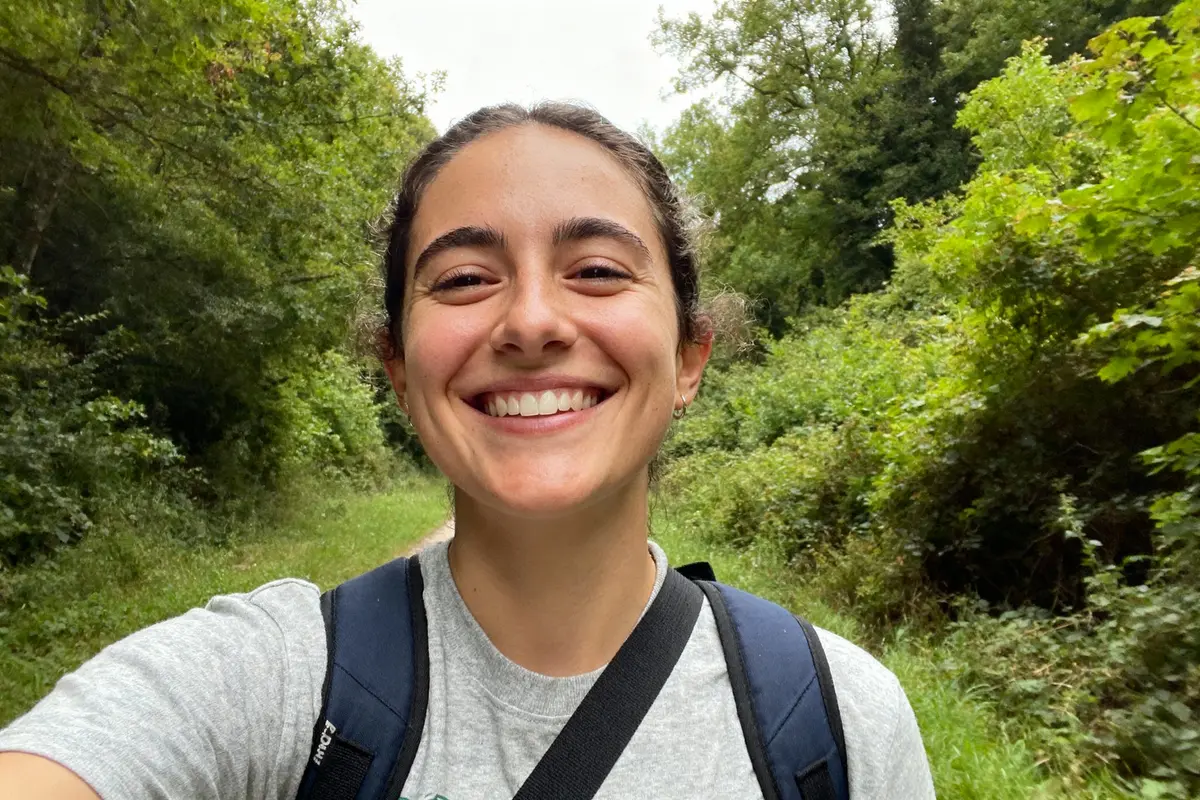 Une personne souriante avec sac à dos dans un chemin forestier verdoyant.
