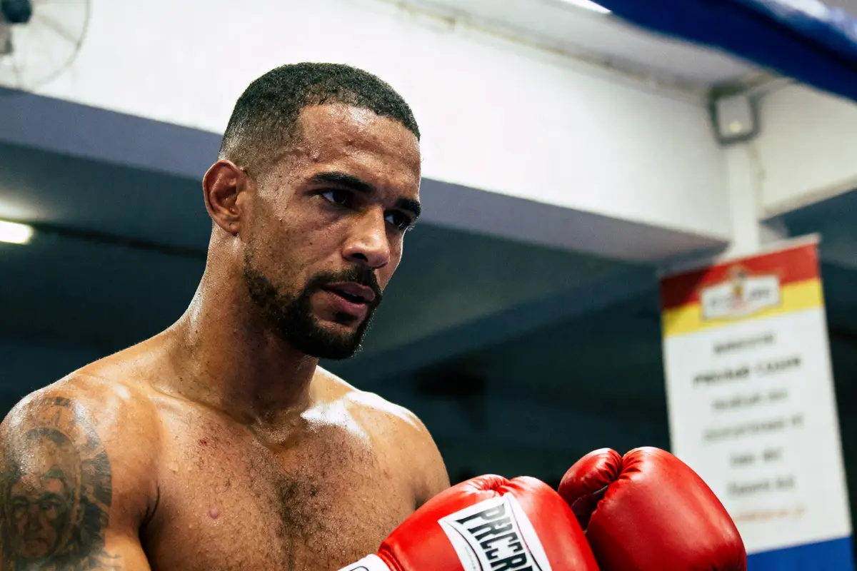 Boxeur torse nu avec gants rouges, concentré durant l'entraînement, dans une salle de sport.