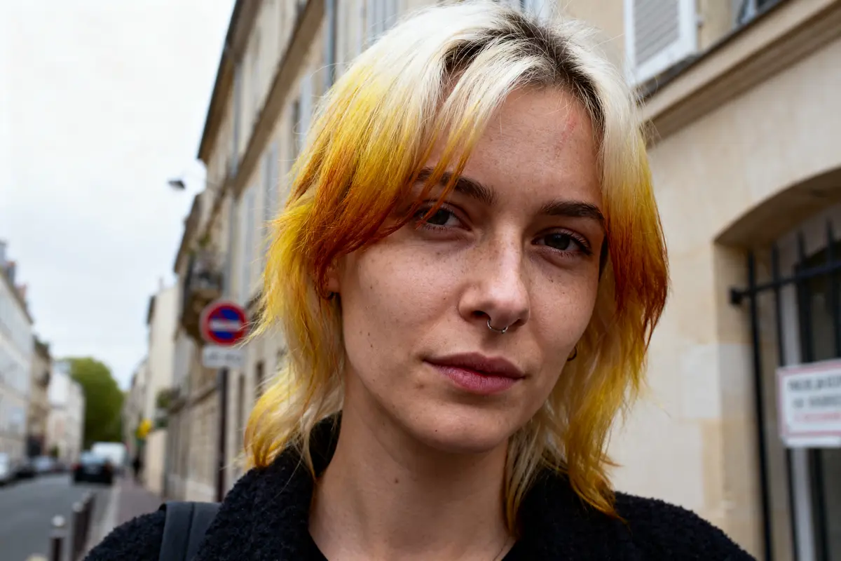 Personne aux cheveux teintés colorés, piercing au nez, pose dans une rue urbaine.