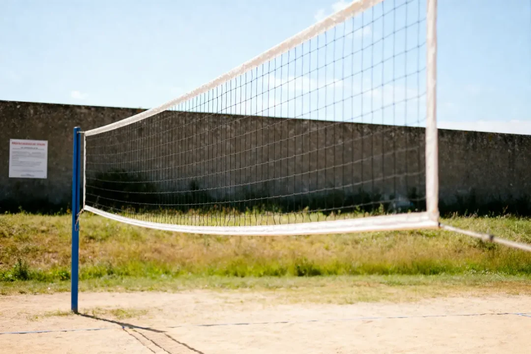Terrain de volley-ball en plein air avec filet, sur sol sablonneux, sous ciel bleu. Mur en arrière-plan.
