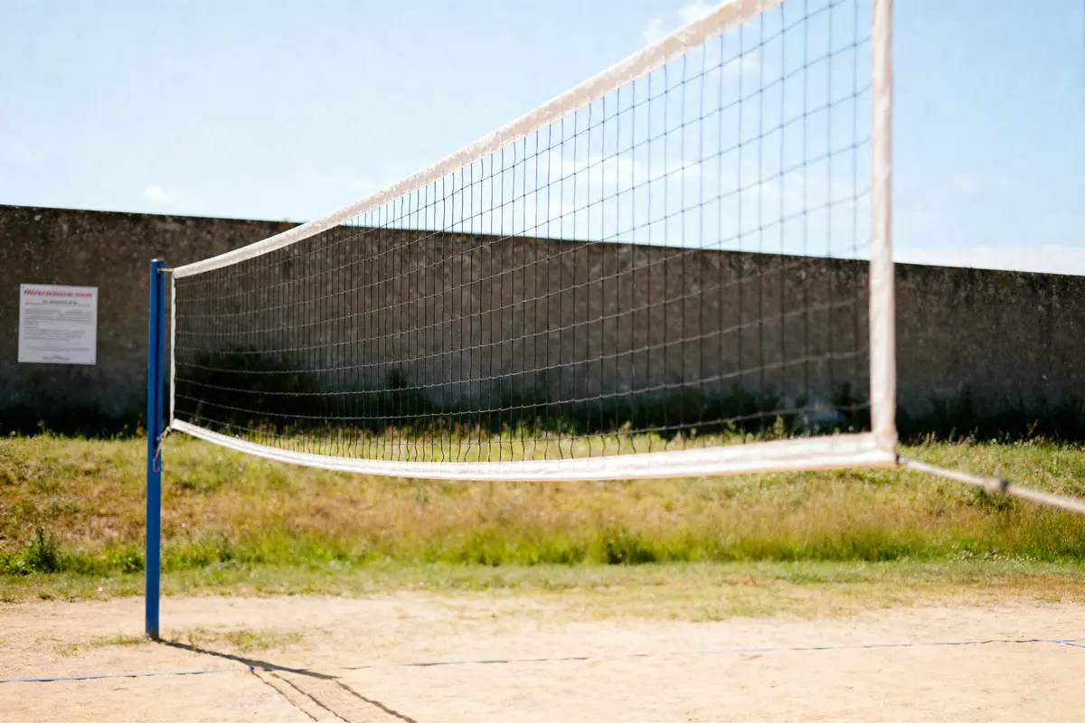 Terrain de volley-ball en plein air avec filet, sur sol sablonneux, sous ciel bleu. Mur en arrière-plan.