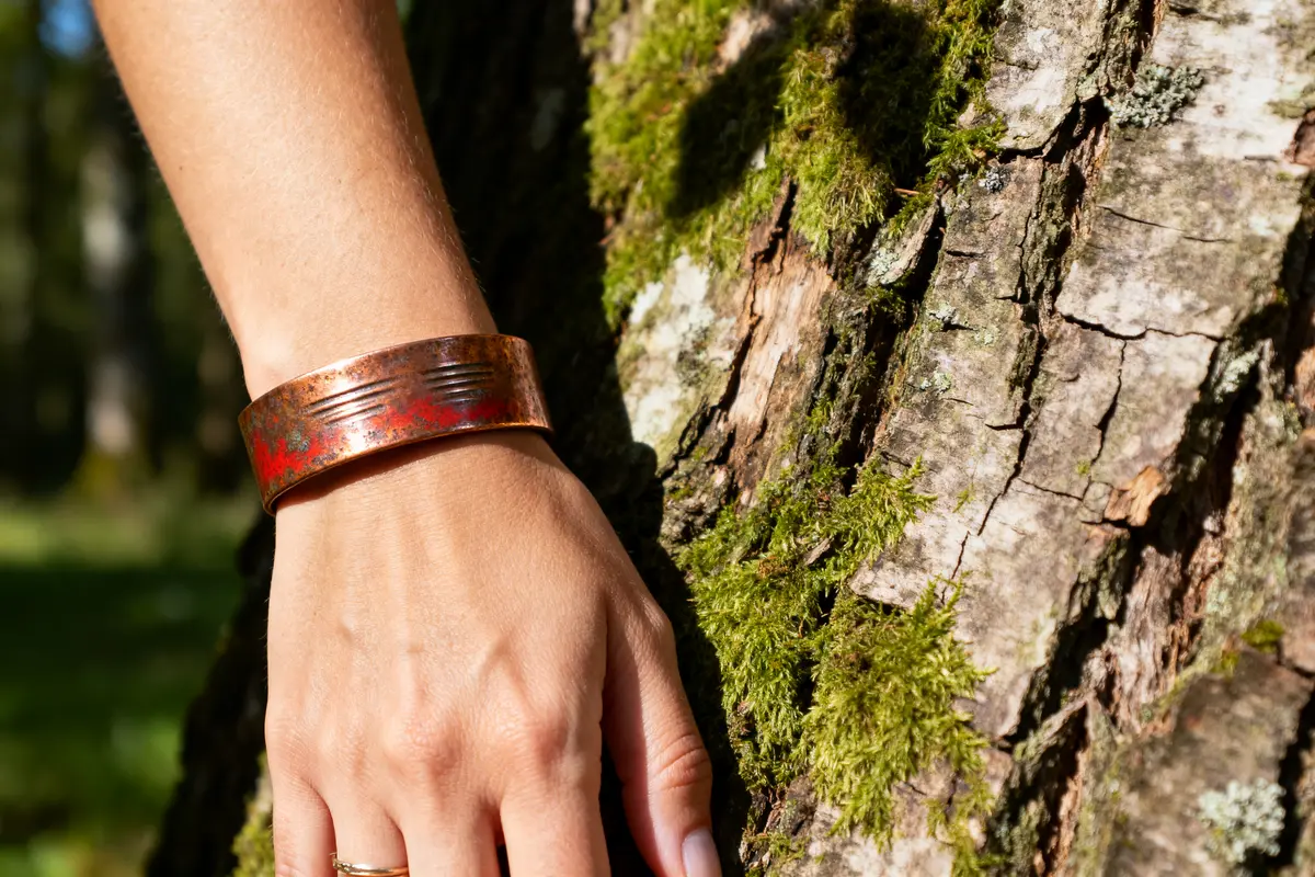 Main portant un bracelet en cuivre contre un arbre illustrant les bienfaits du bracelet en cuivre