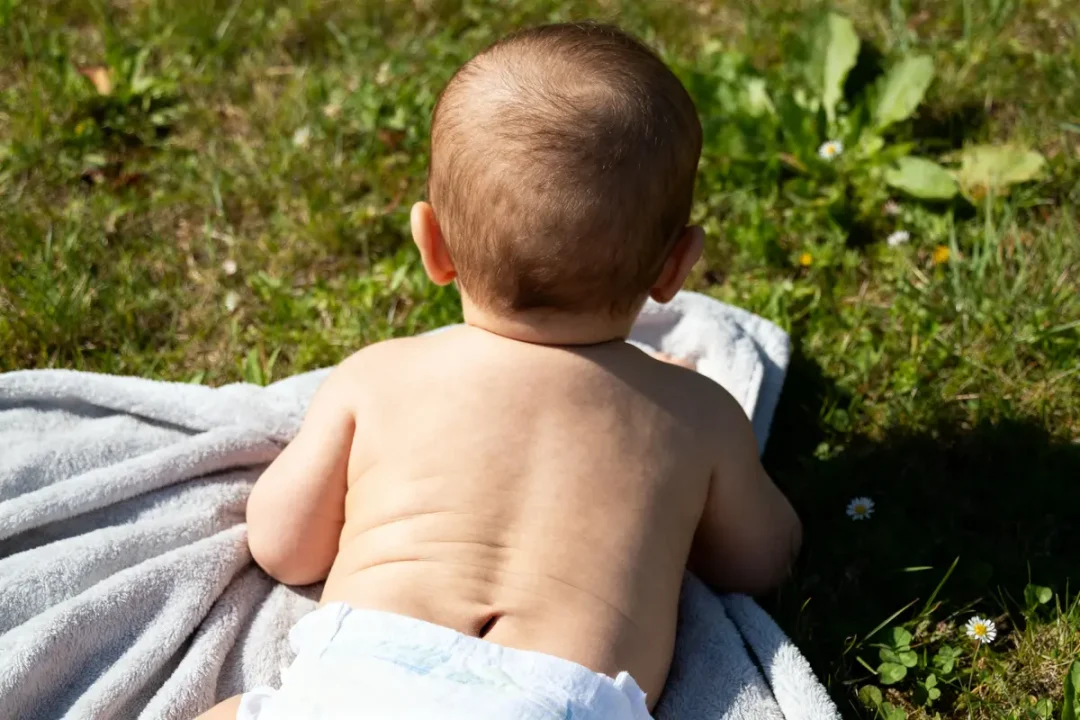 Bébé allongé sur serviette, dos nu avec fossette sacro-coccygienne visible sur l'herbe