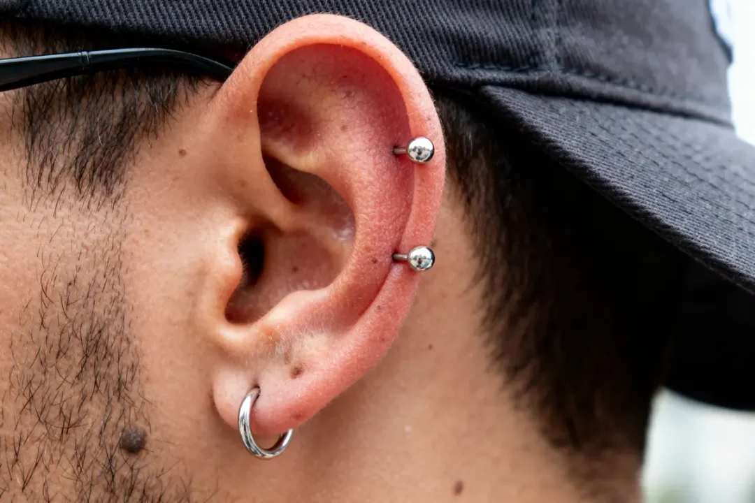 Homme avec casquette et trois piercings d'oreille, évoquant le piercing du capuchon.