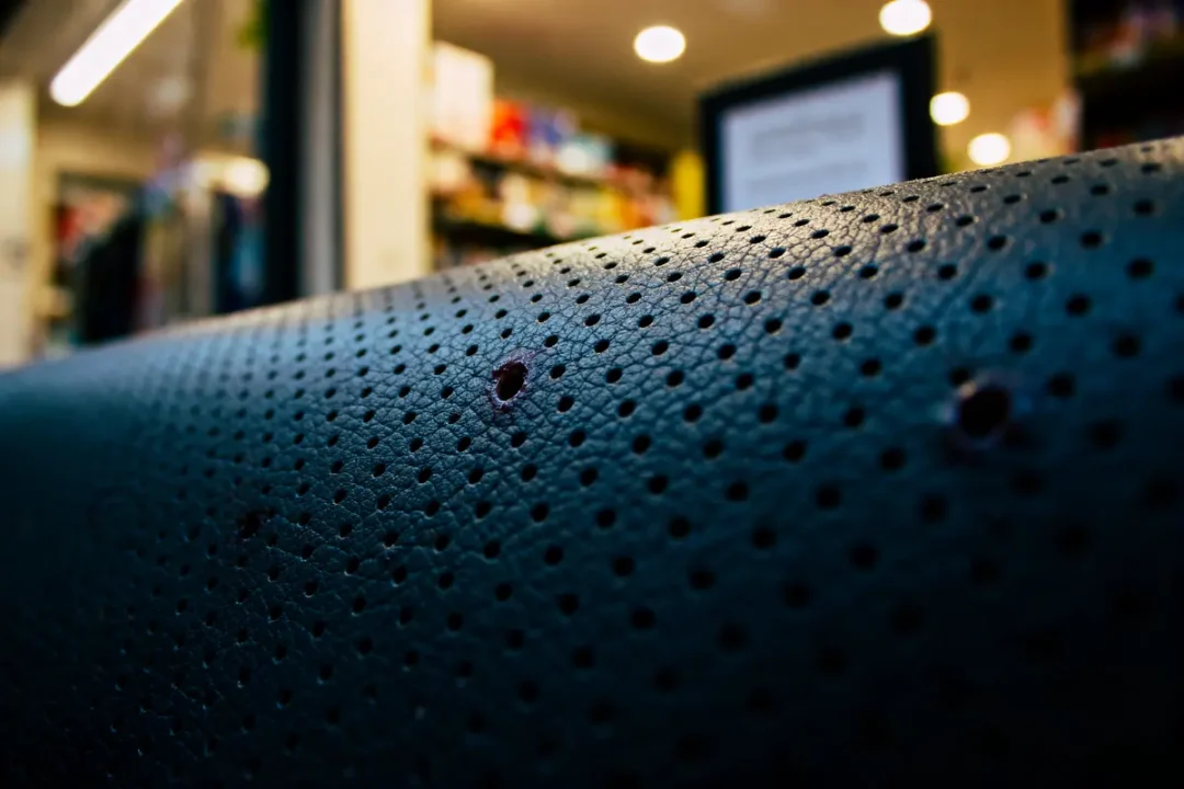 Gros plan sur fauteuil en cuir perforé, intérieur éclairé flou, ambiance chaleureuse et urbaine.